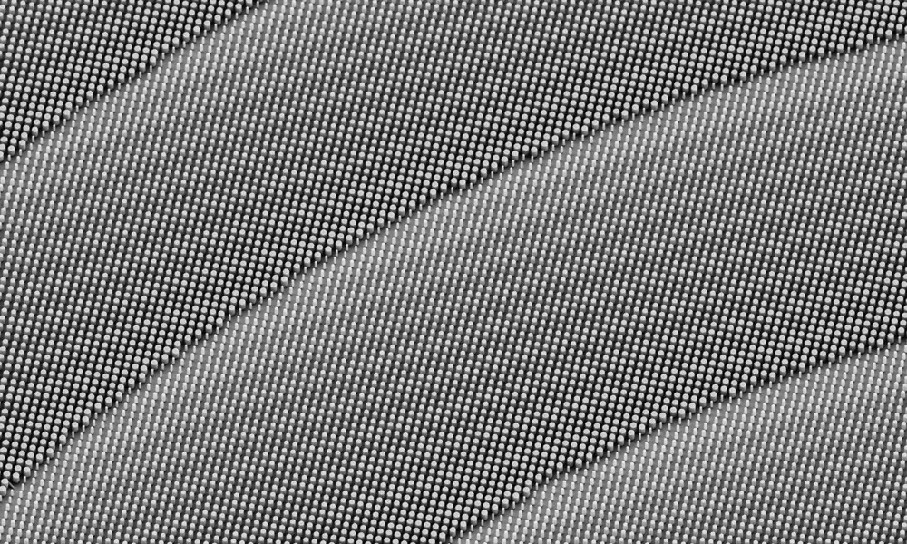 A closeup of a metalens from a scanning electron microscope with four rows of diagonally facing pillars shown. A small bar in the bottom left shows a scale of 1 micrometer.