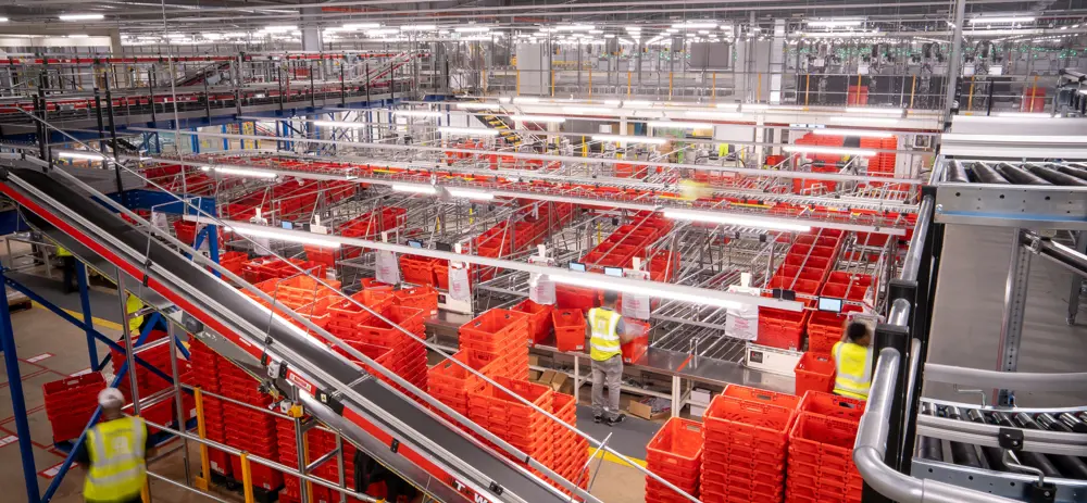 A large amount of plastic crates stacked on top of each other in various columns next to a conveyor belt in a warehouse.