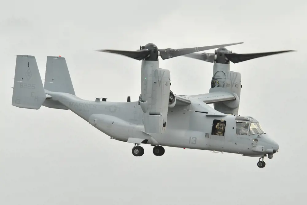 A V-22 Osprey VTOL aircraft in the air, with a marine standing looking out of its side hatch.