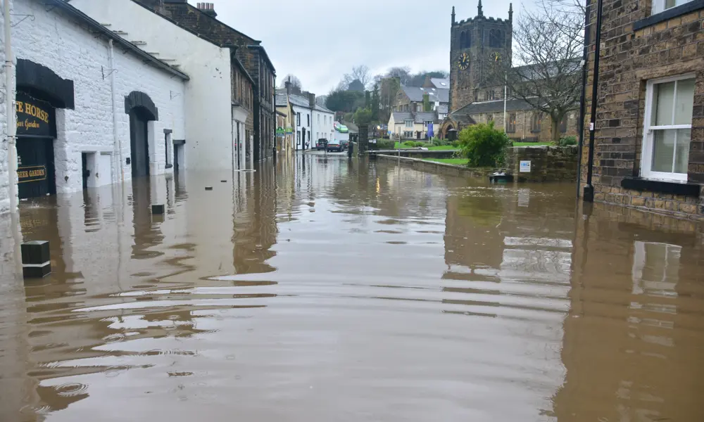 A street in a UK village that has been flooded, with floodwaters rising over a metre from the ground.