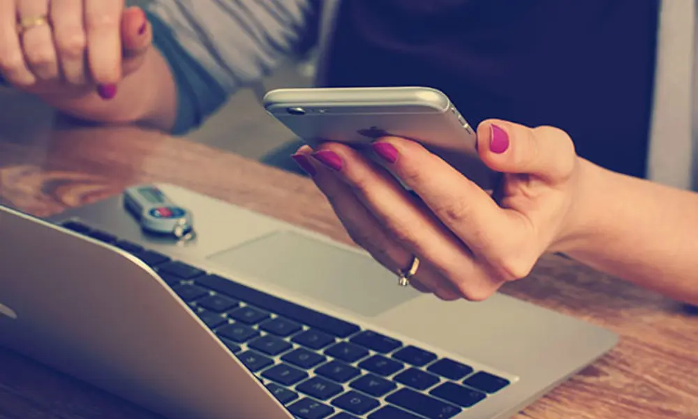 A person holding a phone and using a laptop.