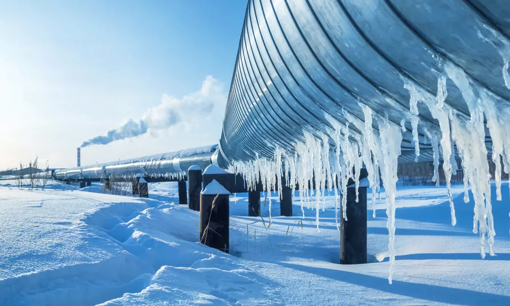A pipeline in the snow, with icicles hanging from it. 