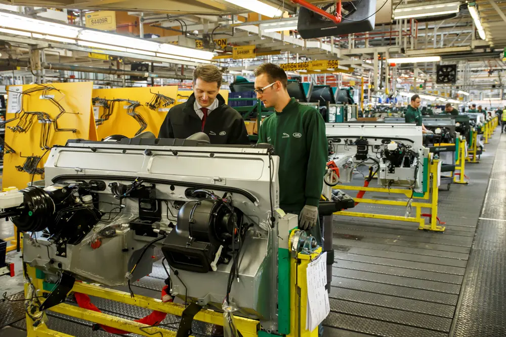 Nick Rogers FREng standing with an engineer, looking at equipment in the Jaguar land rover Defender manufacturing facility.