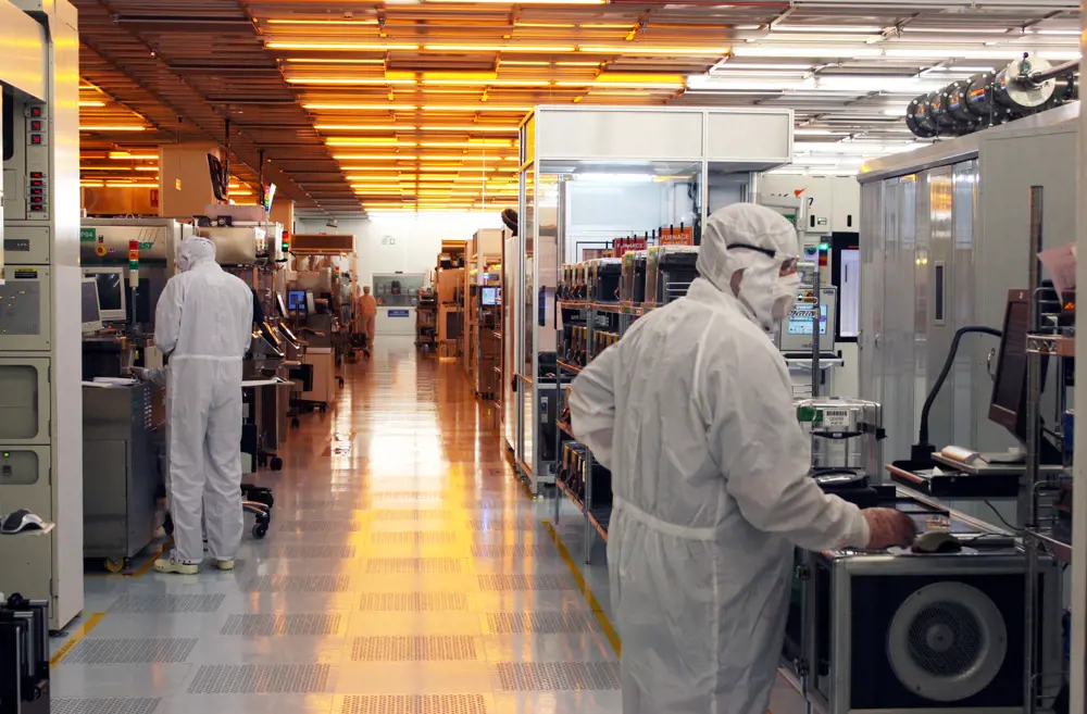 Two scientists wearing cleanroom suits, working in a laboratory that develops semiconductor devices and processes.