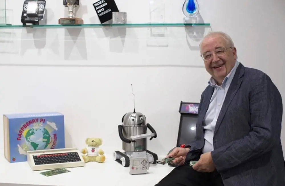 David Cleevely sitting at a desk holding a Raspberry Pi next to a robot.