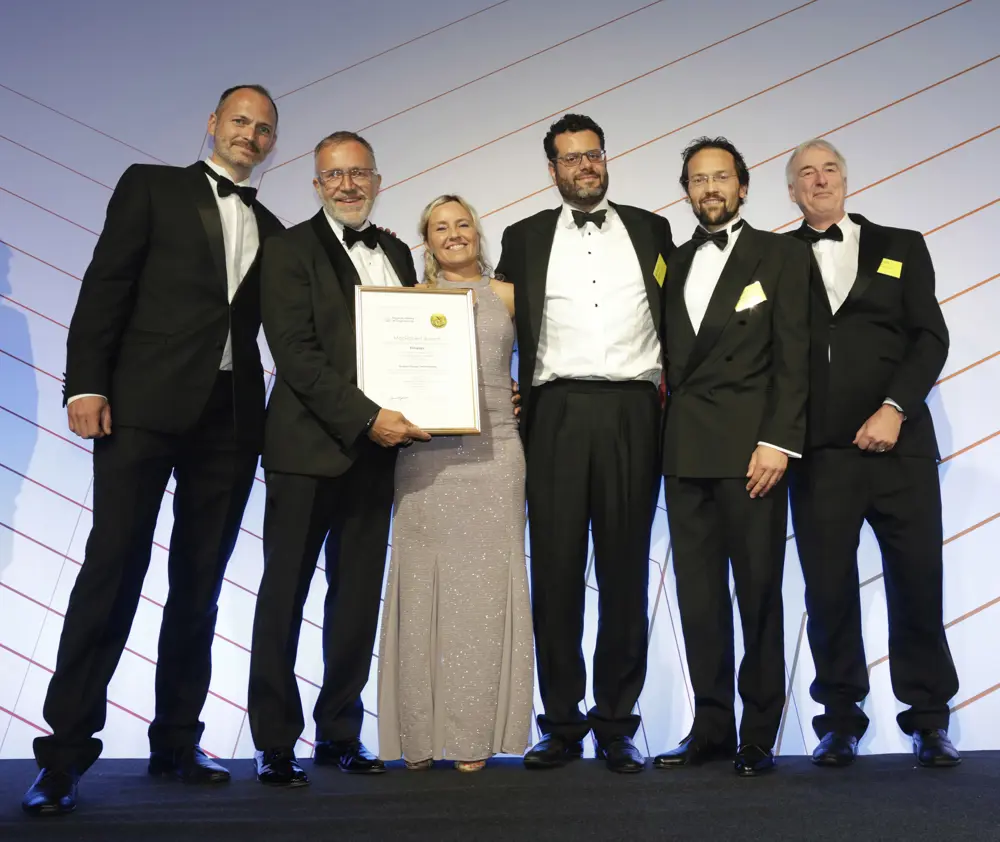 Five men and one woman in smart dress stand on stage with a certificate
