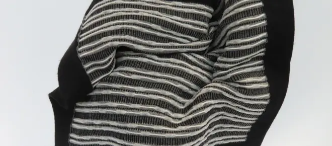 A black fabric woven with over a thousand solar cells, which are seen as a white threaded pattern.