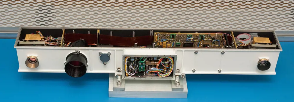 A clean bench with the PanCam engineering model,  showing the wiring and electronic circuits and components inside, 