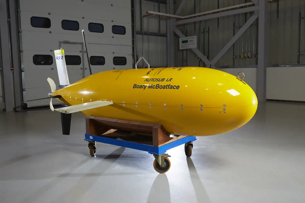 The yellow unmanned robotic autonomous submarine named Boaty McBoatface inside a room. The front is rounded and the back has a propellor.