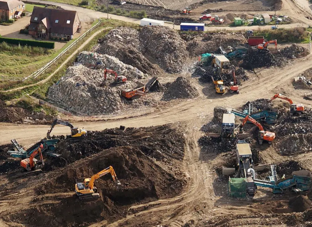 Aerial view of a landfill site, with multiple tractors on different mounds of dirt and waste.
