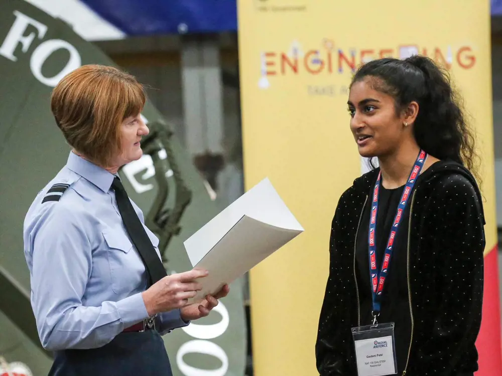 Air Marshal Susan Gray speaking to a young women with an engineering poster in the background. 