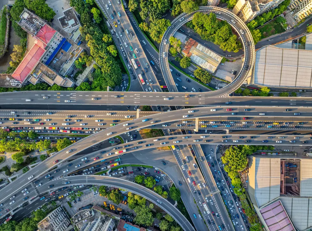 Aerial view of a multi-level highway interchange with heavy traffic and surrounding greenery, illustrating interconnected transport systems.
