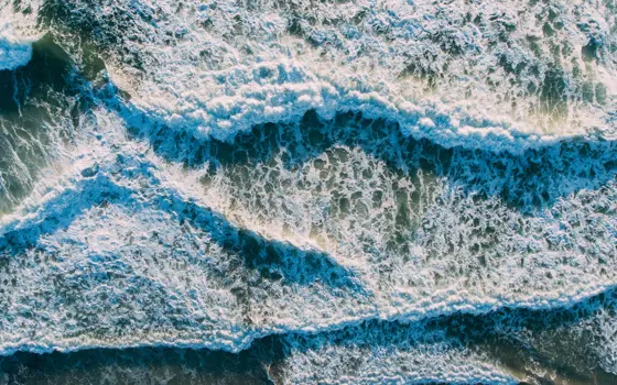 Drone image of tides coming in from the sea, topped with sea foam.