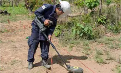A male, wearing a face shield and protective equipment, with a dual-sensor detector in a field.