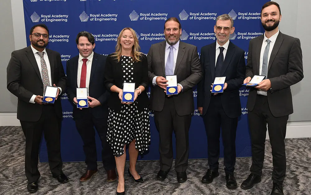 Six individuals standing in front of a Royal Academy of Engineering backdrop, each holding an award medal in a presentation box.