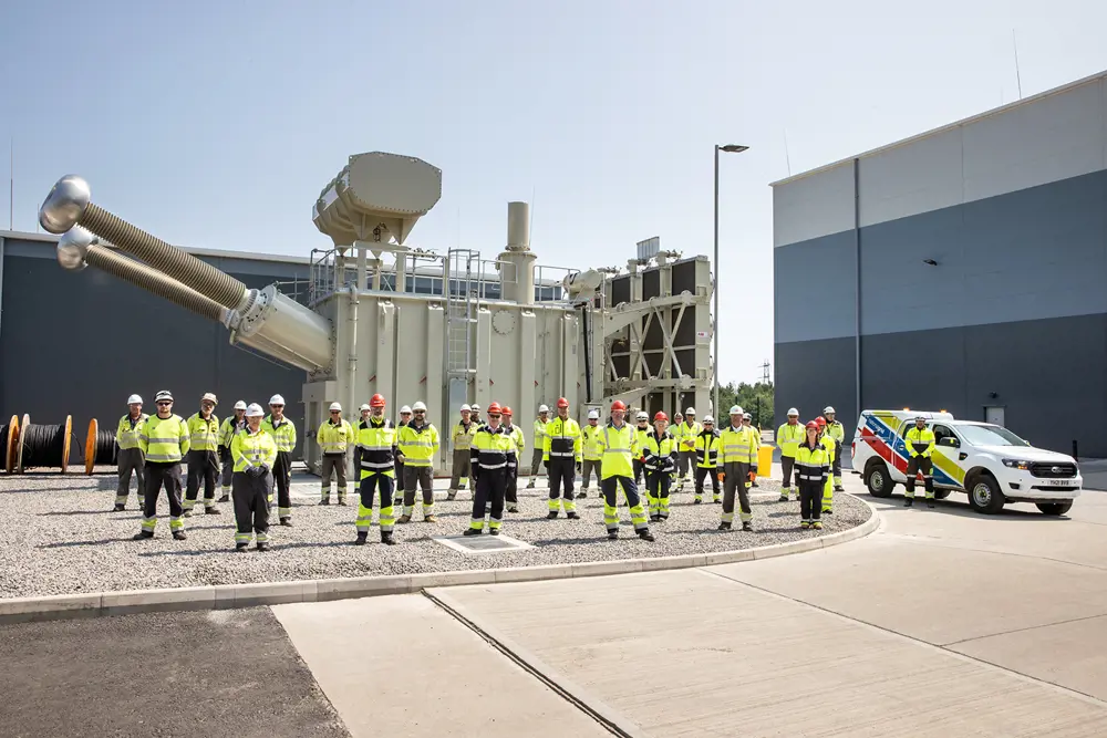 A group of people wearing high vis clothing and hard hats stand outside in front of a large piece of silver machinery