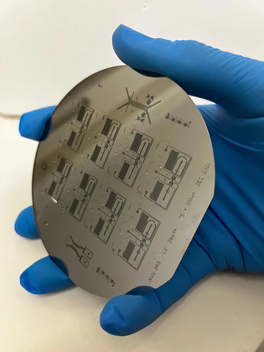 A gloved hand holding a patterned silicon wafer to be used to imprint microchannels of an organ on a chip in a soft polymer.