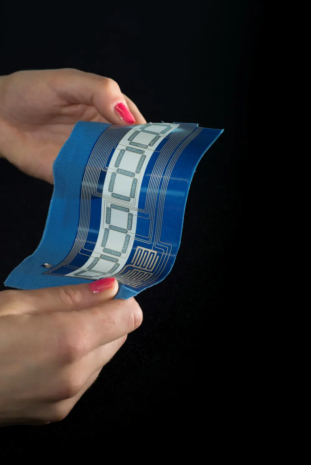 A pair of hands bending a sample of blue fabric, about the size of a smartphone, with a shiny circuit printed onto it.