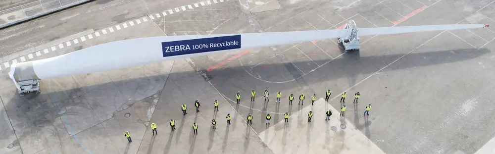 An aerial photograph of a turbine blade with the letters 'ZEBRA 100% recyclable' printed on and 26 people in yellow jackets standing in the shape of a blade in front.