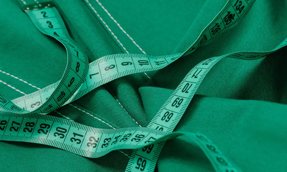 A green tape measure lying on top of green-coloured denim