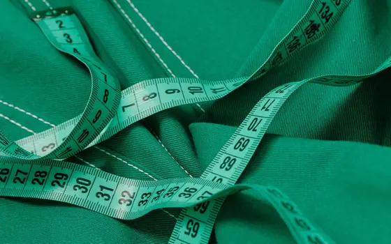 A green tape measure lying on top of green-coloured denim