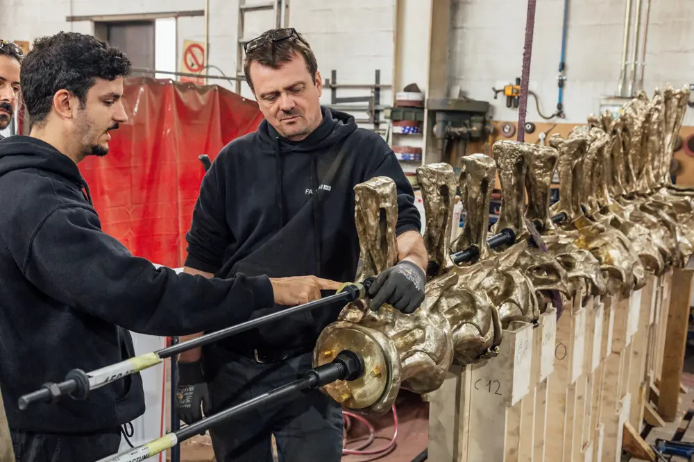 Three men handling and discussing the bronze cast spine of the sauropod sculture