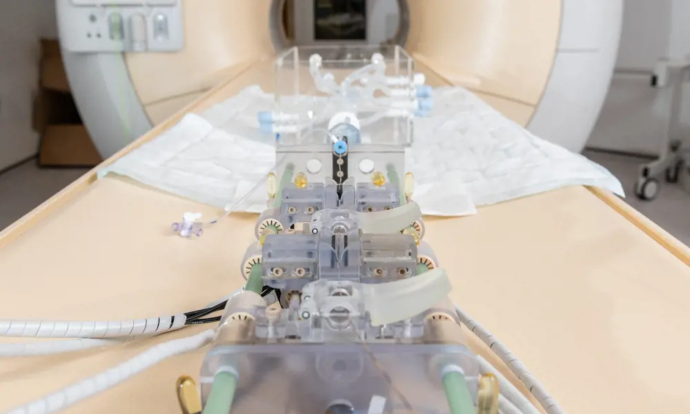 A robot on a CT scanner patient table, which has wires and tubing to adjust guidewires and catheters.