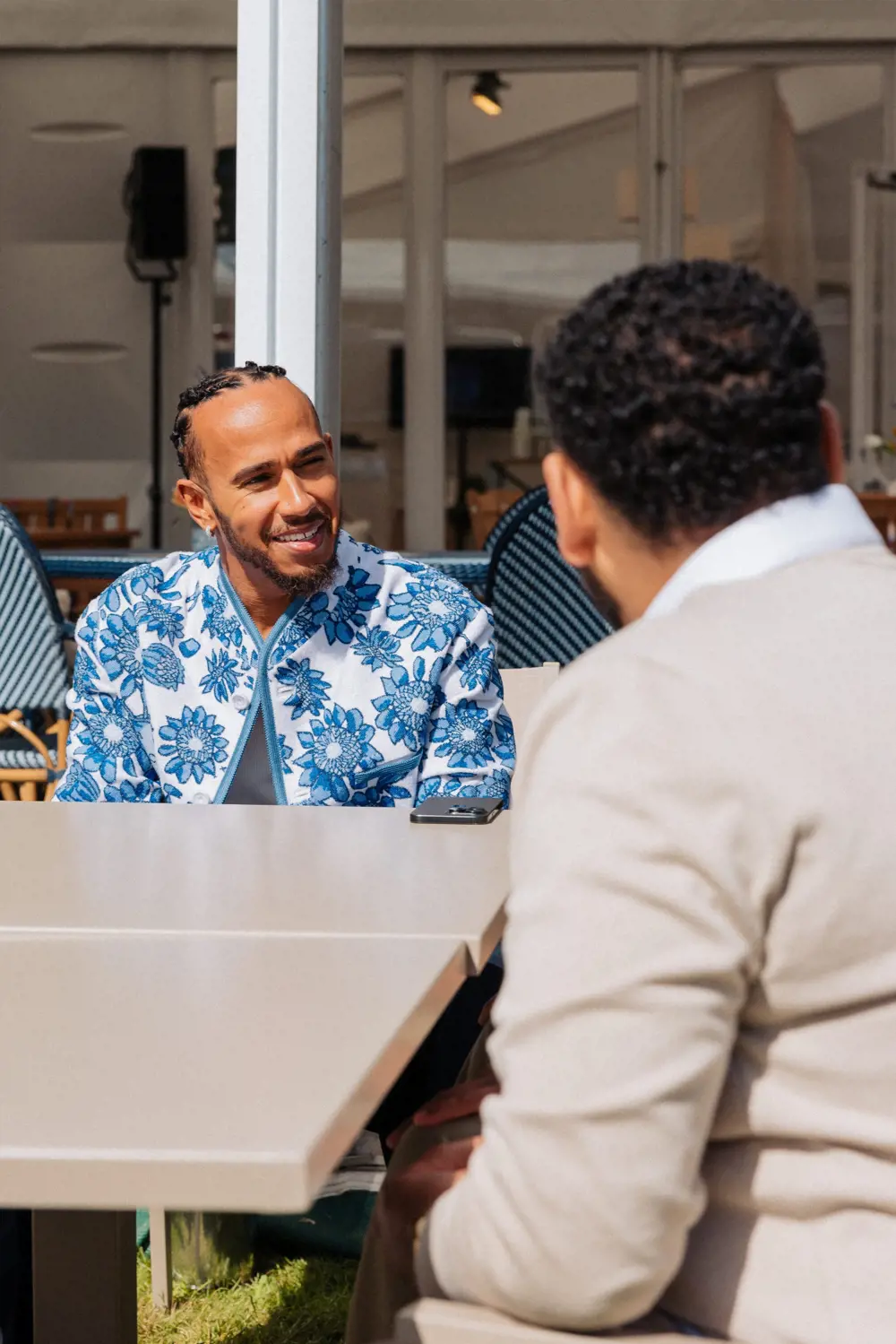 Lewis Hamilton wearing a blue floral jacket, smiling in conversation with Amjad.