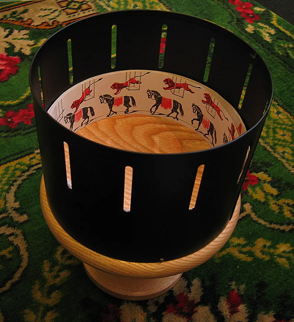 A zoetrope, with the image displayed inside an animation of a lion leaping at a horse in a circus environment.
