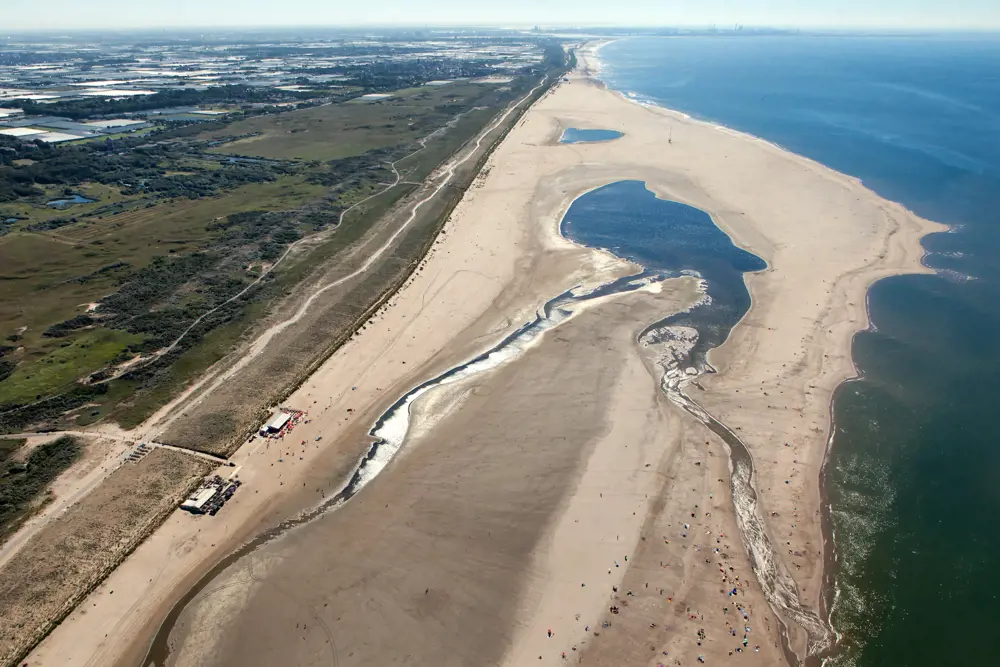 An aerial image above De Zandmotor in the Hague. The beach is much wider than further down the coast, and has a windsurfing lake in the middle.