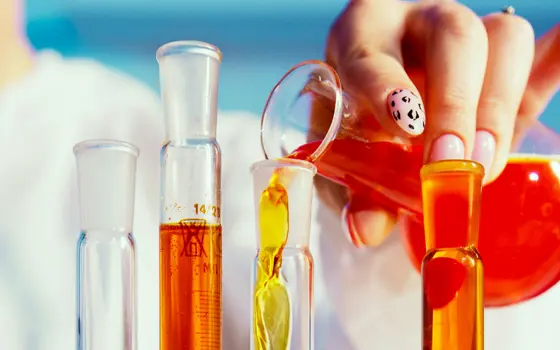 A manicured hand pouring chemicals into lab glassware.