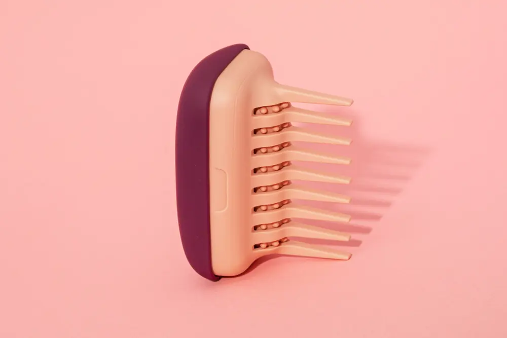 A specialist detangler comb in front of a peach background.