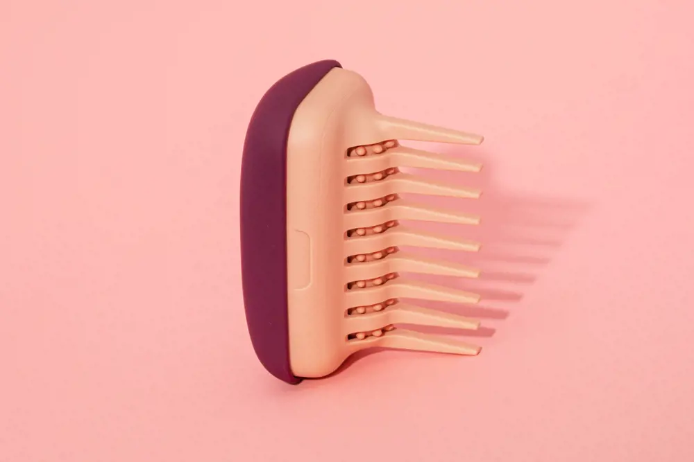 A specialist detangler comb in front of a peach background.